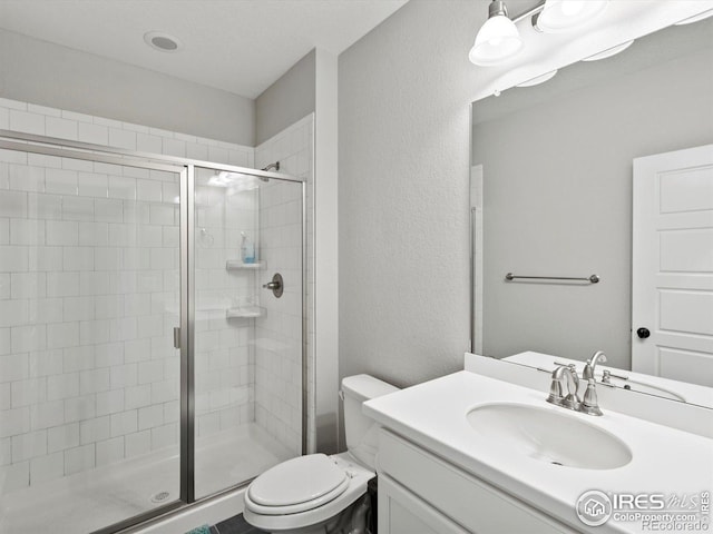 full bathroom with toilet, a textured wall, a shower stall, and vanity