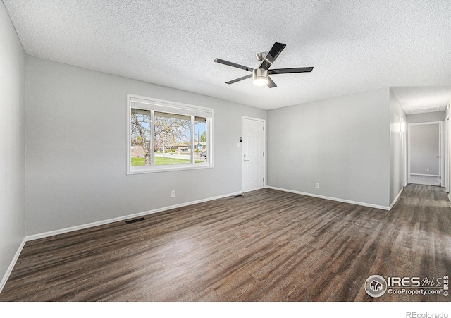 spare room featuring a textured ceiling, visible vents, dark wood-style floors, and baseboards