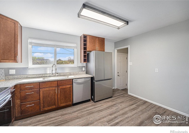 kitchen with brown cabinets, appliances with stainless steel finishes, a sink, light wood finished floors, and baseboards