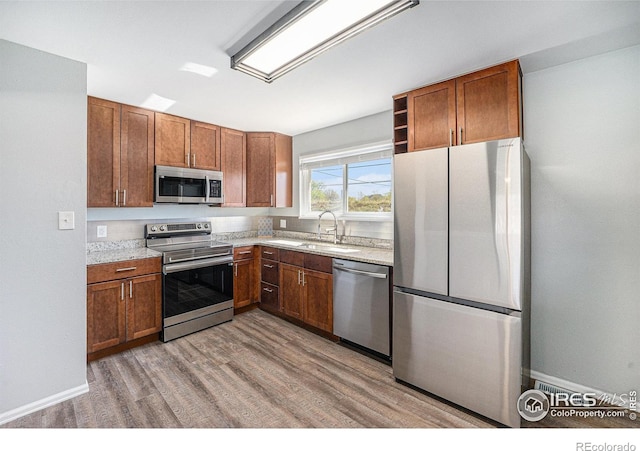 kitchen with a sink, wood finished floors, brown cabinets, and stainless steel appliances