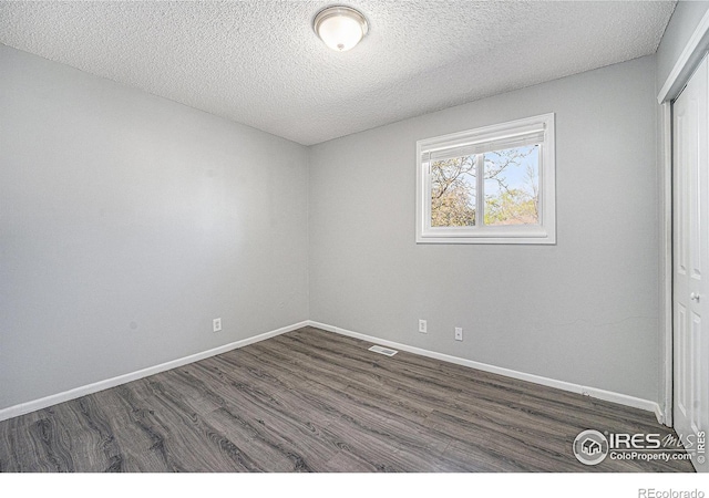 spare room featuring baseboards, dark wood-type flooring, a textured ceiling, and visible vents