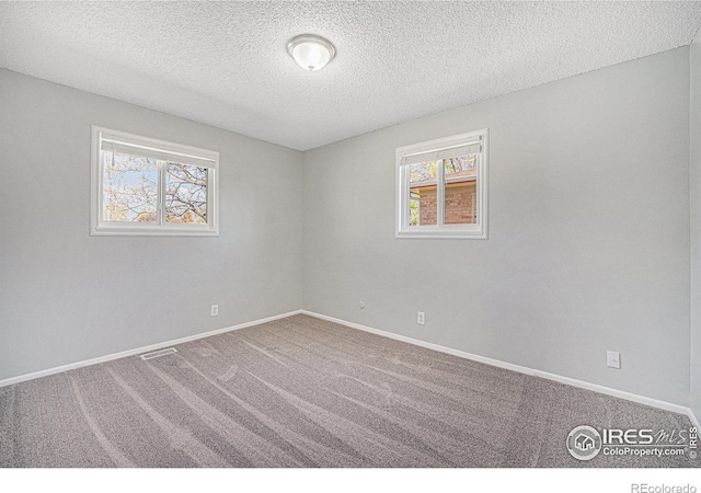 carpeted empty room with a healthy amount of sunlight, baseboards, and a textured ceiling