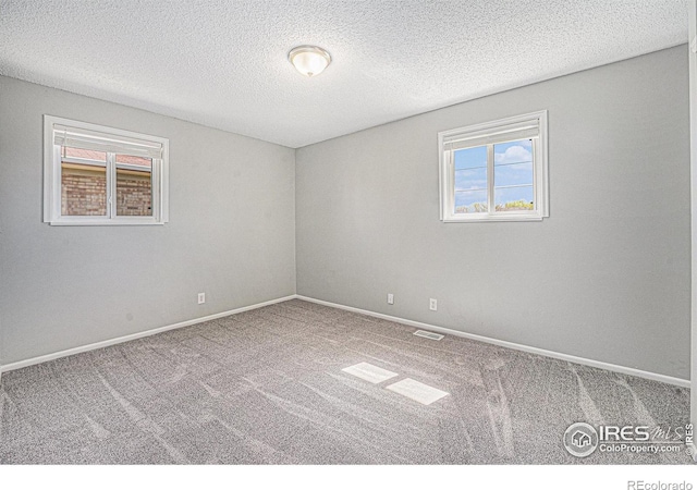 carpeted spare room featuring plenty of natural light, baseboards, and visible vents