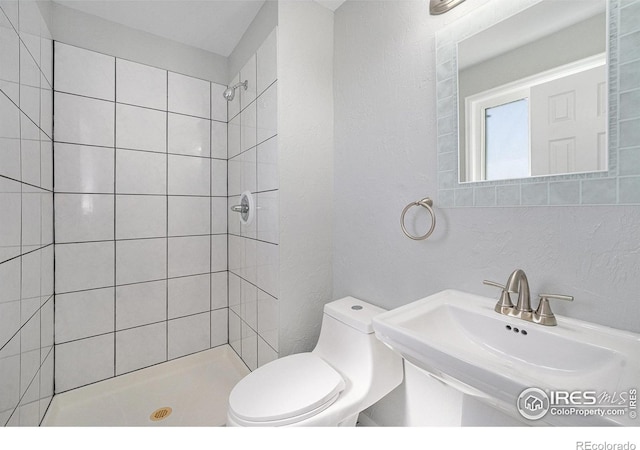 full bathroom with toilet, tiled shower, and a sink