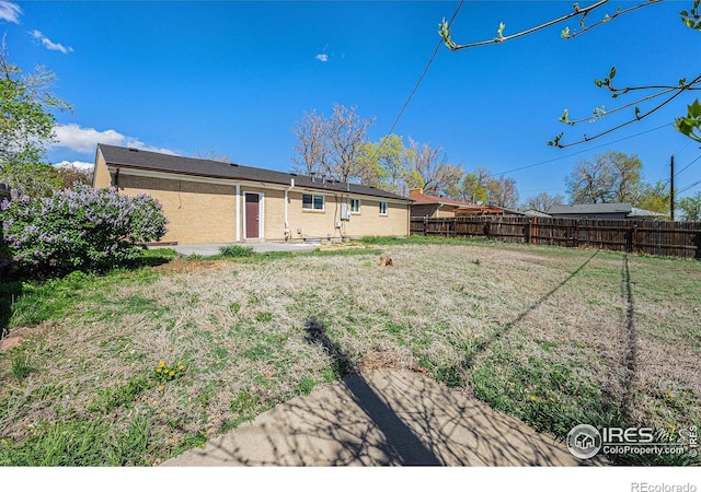 back of house featuring a patio, a lawn, fence, and brick siding