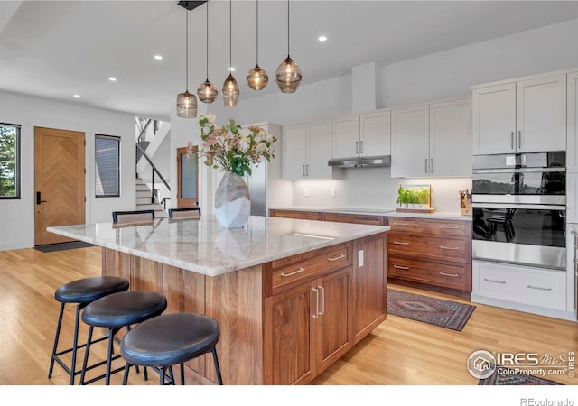 11 Juneau Cir, Nederland, CO 80466 - kitchen featuring a breakfast bar area, under cabinet range hood, cooktop, light wood-style flooring, and hanging light fixtures