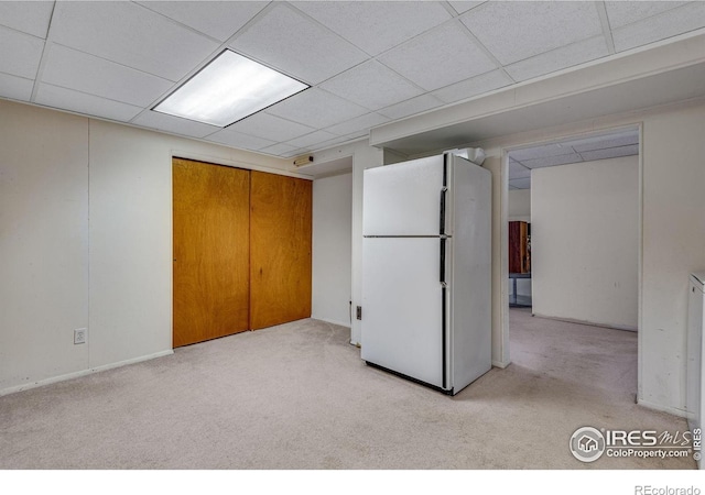 finished below grade area featuring freestanding refrigerator, light carpet, and a drop ceiling