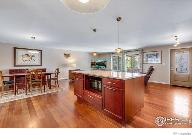 kitchen with wood finished floors, baseboards, black microwave, and pendant lighting