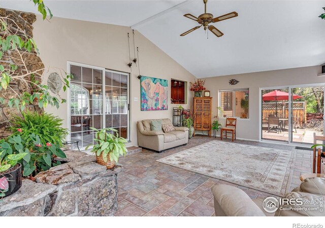 living area with ceiling fan, beamed ceiling, high vaulted ceiling, stone finish flooring, and baseboards