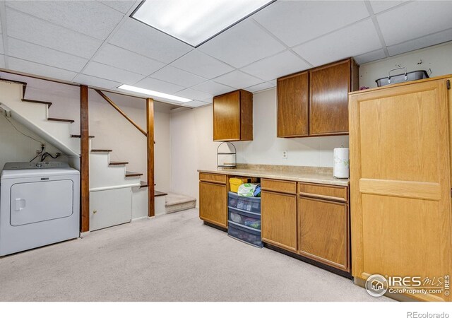 kitchen with washer / dryer, light colored carpet, a paneled ceiling, light countertops, and brown cabinets