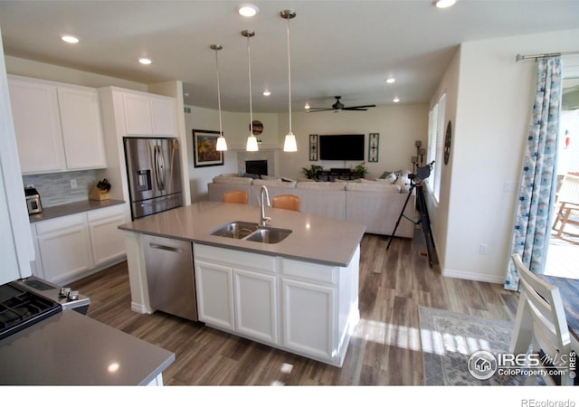 kitchen featuring appliances with stainless steel finishes, a sink, a ceiling fan, open floor plan, and wood finished floors