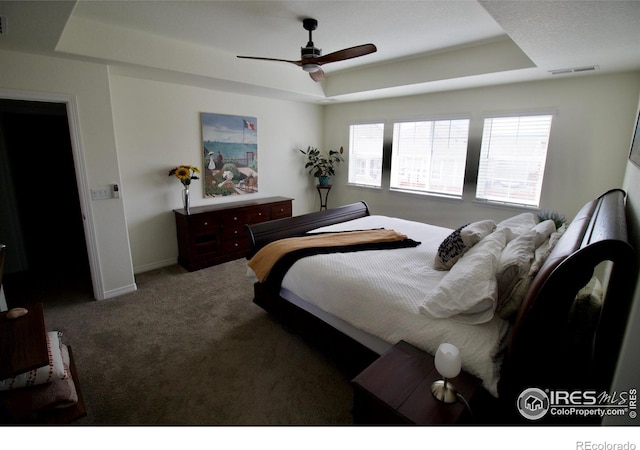 carpeted bedroom featuring a ceiling fan, a tray ceiling, visible vents, and baseboards