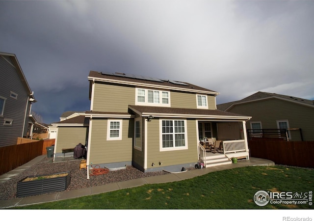 rear view of house featuring a lawn, covered porch, solar panels, and a fenced backyard