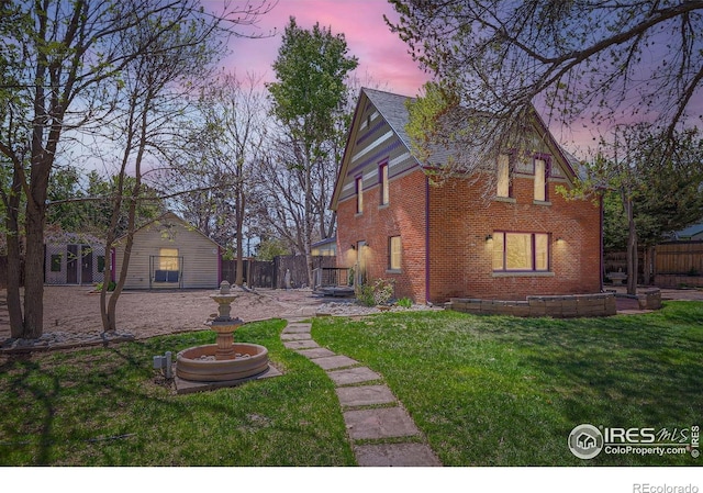 rear view of house with a lawn, an outdoor structure, fence, and brick siding