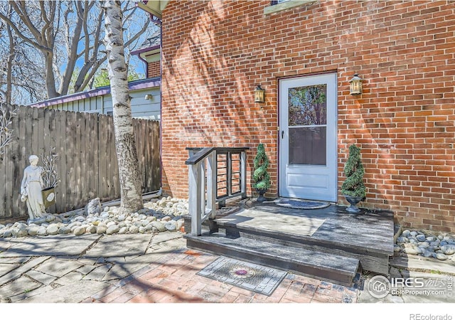 view of exterior entry with brick siding and fence
