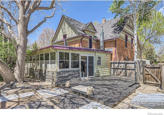 rear view of house featuring fence, brick siding, a sunroom, a gate, and a chimney