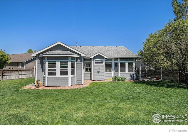 back of house featuring a lawn, a shingled roof, and a fenced backyard