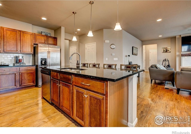 kitchen with stainless steel appliances, open floor plan, a sink, and light wood-type flooring