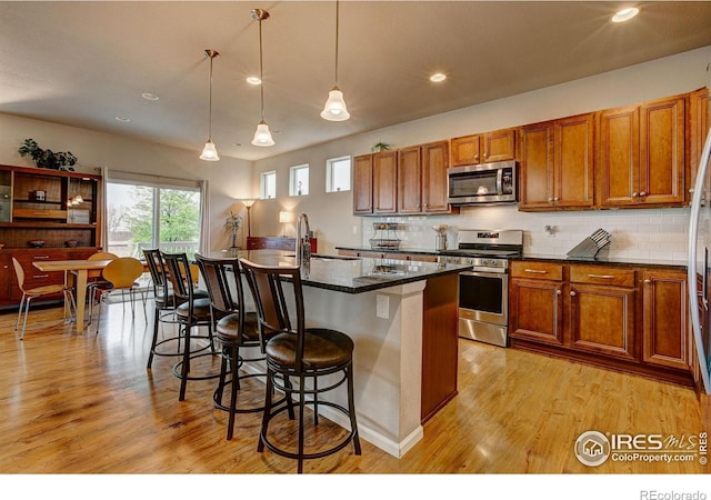 kitchen with light wood-style floors, a breakfast bar area, brown cabinetry, stainless steel appliances, and decorative backsplash
