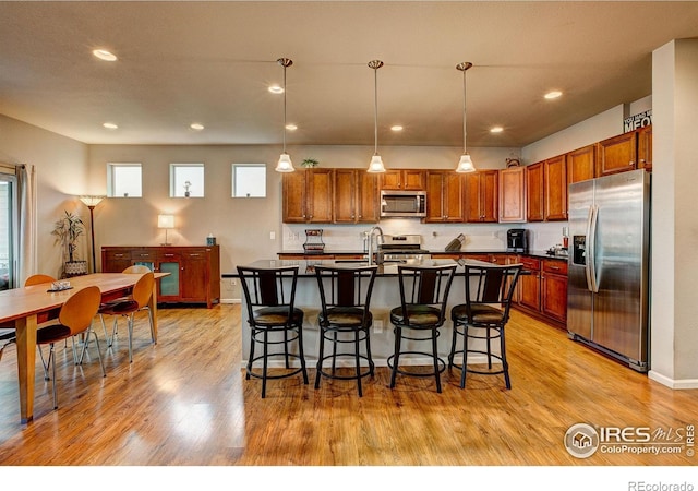 kitchen with stainless steel appliances, dark countertops, light wood-type flooring, and a kitchen bar