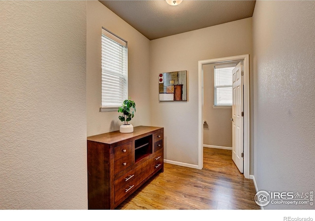 hall featuring baseboards, a textured wall, and light wood-style flooring