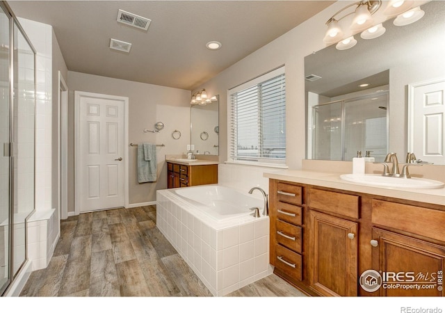 full bathroom with visible vents, wood finished floors, a bath, a sink, and a stall shower