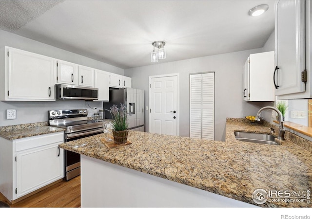 1309 Alexandria St, Lafayette, CO 80026 - kitchen with appliances with stainless steel finishes, a sink, white cabinetry, light wood-style floors, and a peninsula