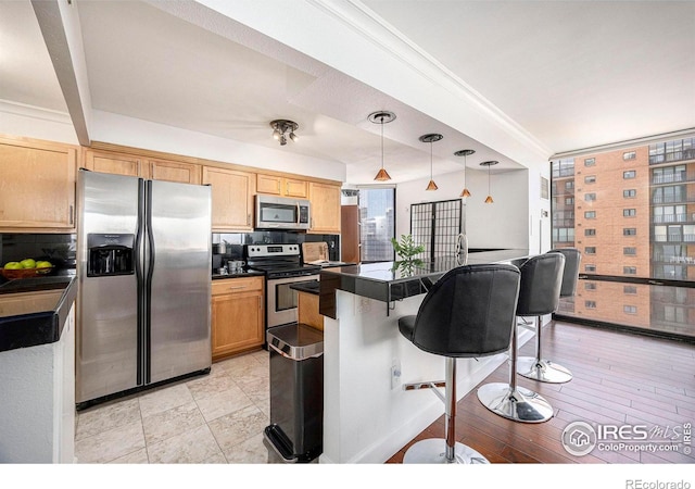 kitchen featuring a kitchen bar, decorative light fixtures, dark countertops, appliances with stainless steel finishes, and a center island