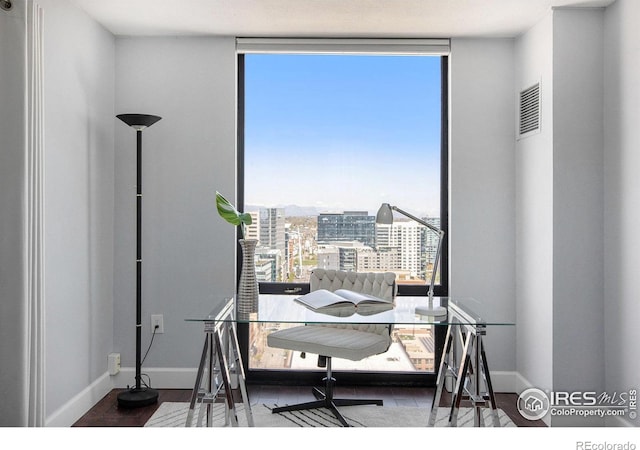 office area featuring a view of city, baseboards, visible vents, and expansive windows