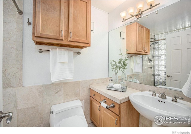 full bath featuring a tile shower, a sink, toilet, a wainscoted wall, and tile walls