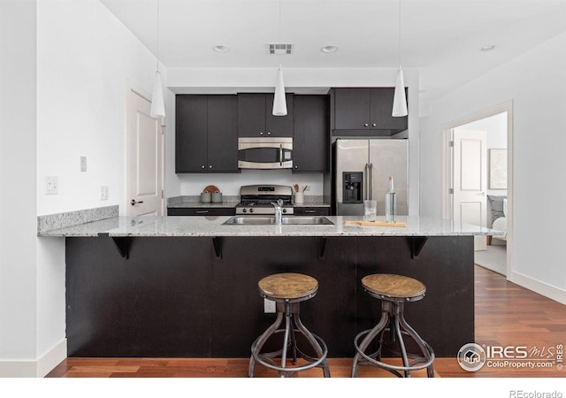 2001 Lincoln St Unit 2113, Denver, CO 80202 - kitchen featuring appliances with stainless steel finishes, a breakfast bar area, dark wood finished floors, dark cabinetry, and hanging light fixtures