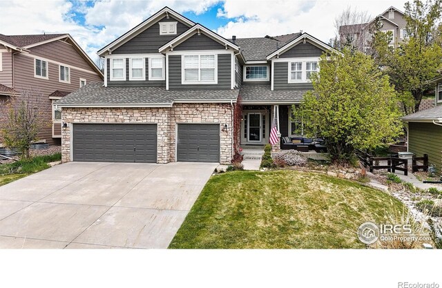 craftsman-style home featuring roof with shingles, stone siding, a garage, a front yard, and driveway
