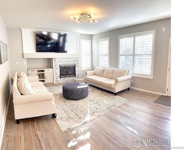 living area with baseboards, wood finished floors, and a stone fireplace