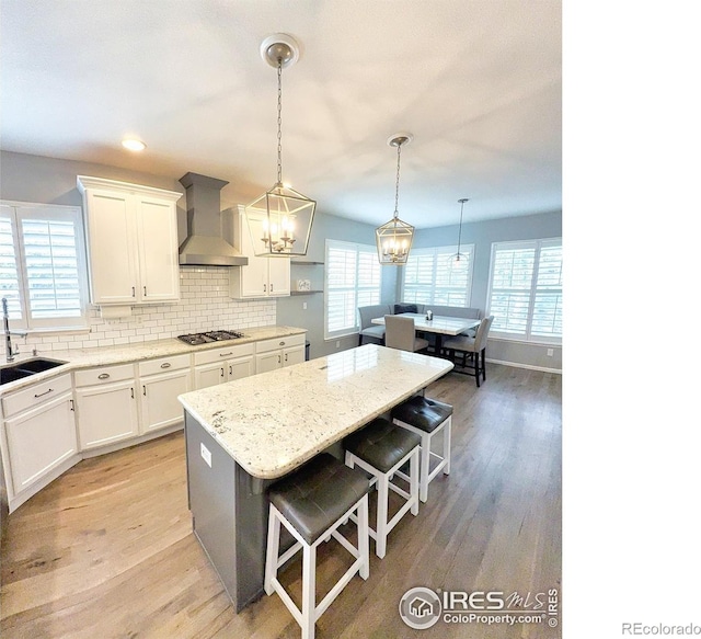 kitchen featuring a kitchen breakfast bar, white cabinets, wall chimney range hood, and stainless steel gas stovetop