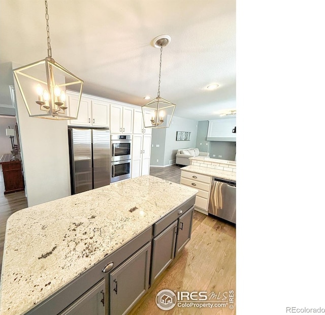 kitchen with a chandelier, appliances with stainless steel finishes, light stone countertops, open floor plan, and light wood-style floors