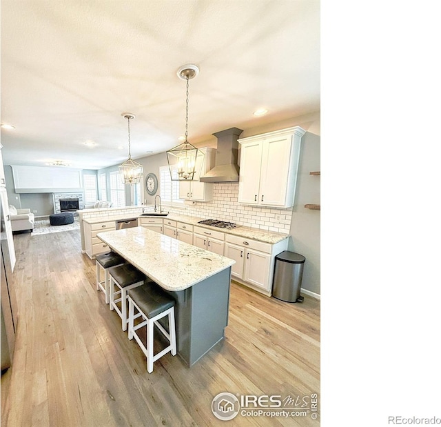 kitchen with a sink, a fireplace with raised hearth, a peninsula, stainless steel gas stovetop, and wall chimney exhaust hood