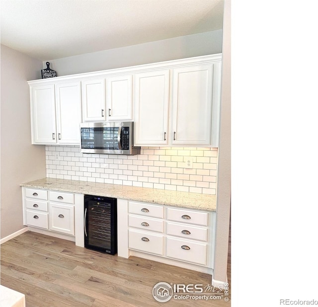kitchen with wine cooler, decorative backsplash, stainless steel microwave, and white cabinetry