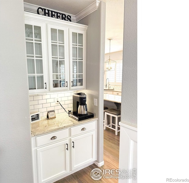 bar featuring backsplash, crown molding, pendant lighting, a sink, and light wood-style floors