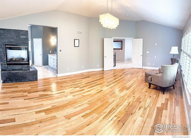 living room with light wood-type flooring, a multi sided fireplace, vaulted ceiling, and visible vents