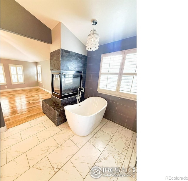 full bathroom featuring marble finish floor, lofted ceiling, a soaking tub, and tile walls