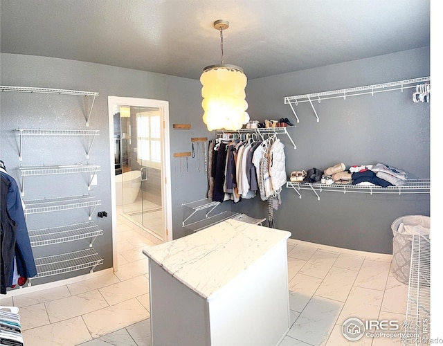 spacious closet featuring an inviting chandelier and marble finish floor