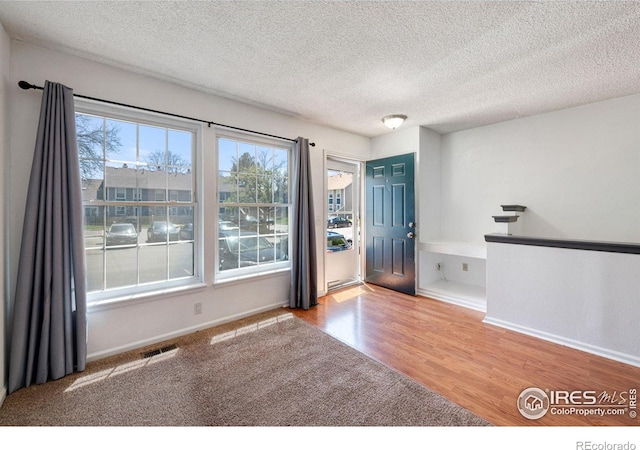 spare room with visible vents, baseboards, a textured ceiling, and wood finished floors