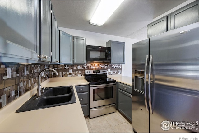 kitchen featuring light tile patterned flooring, a sink, light countertops, stainless steel appliances, and backsplash