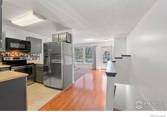 kitchen with decorative backsplash, light tile patterned flooring, light countertops, a textured ceiling, and appliances with stainless steel finishes