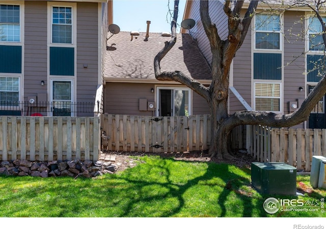 back of house featuring a lawn, a shingled roof, and fence