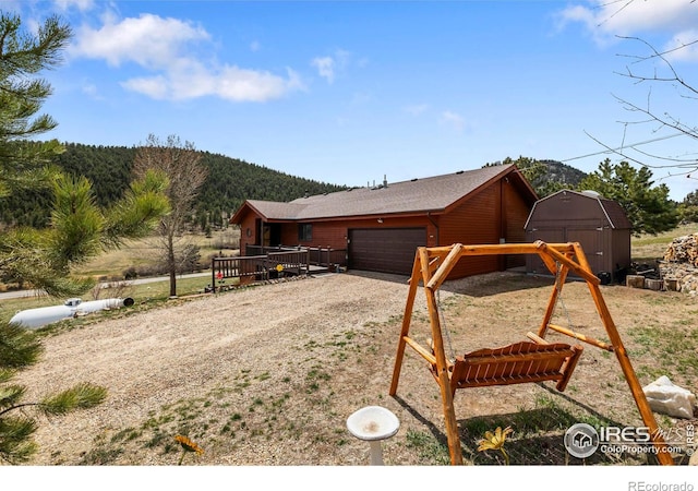exterior space featuring a storage shed, an attached garage, a mountain view, driveway, and an outbuilding