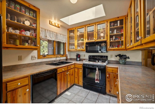 kitchen with a sink, brown cabinetry, a skylight, black appliances, and light tile patterned flooring