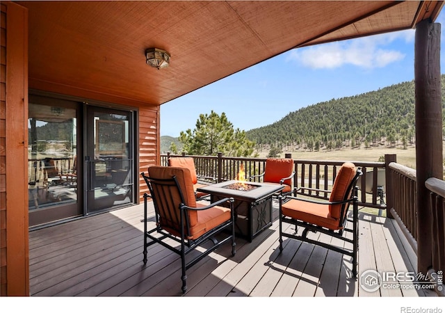 wooden deck with an outdoor fire pit, a view of trees, and a mountain view