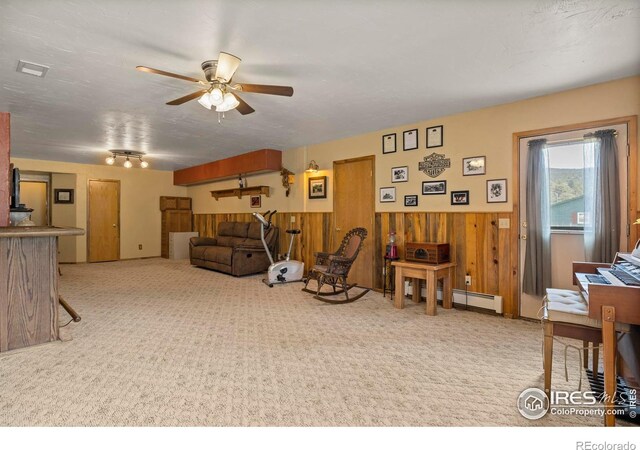 living area with ceiling fan, wood walls, carpet flooring, and baseboard heating