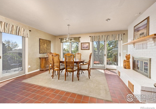 dining area with tile patterned flooring, a chandelier, and a brick fireplace